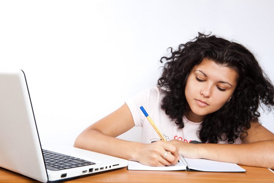 Student at their laptop working on an assignment and taking notes